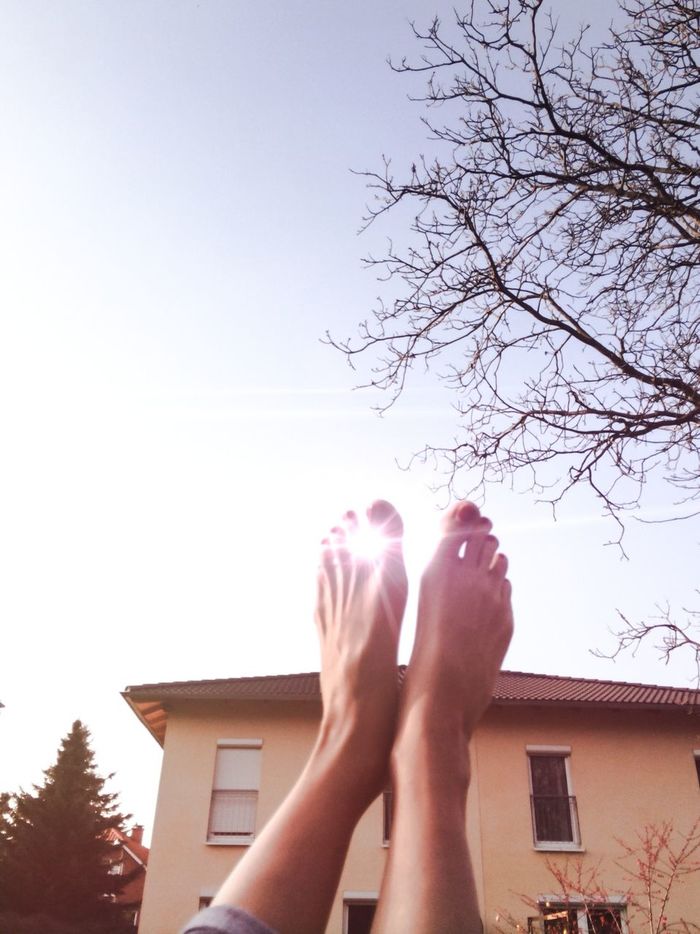 Close-up low section of bare feet against the sky