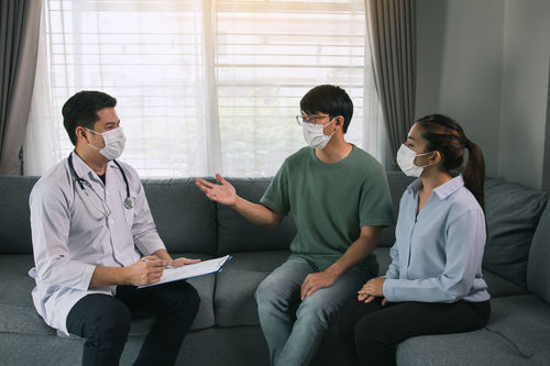 Young couple wearing mask having discussion with doctor at home