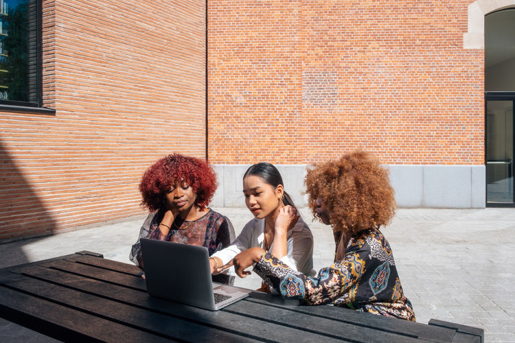Multiracial female students sitting outdoor the university using a laptop computer 