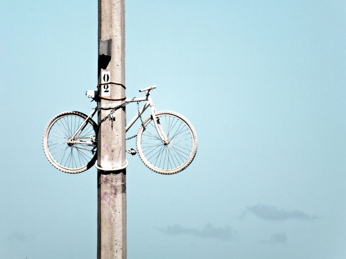 Low angle view of bicycle locked on pole against sky