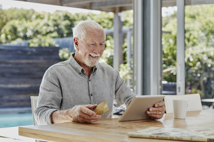 Senior man sitting on terrace, doing online payment with credit card
