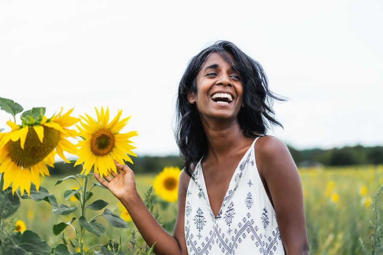 Portrait of young woman standing amidst sunflower against sky