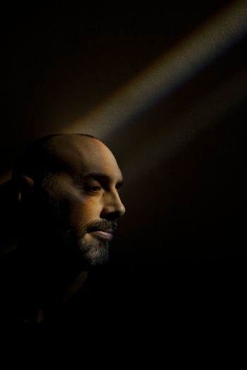 Man sitting in a rainbow beam along a dark wall in basement