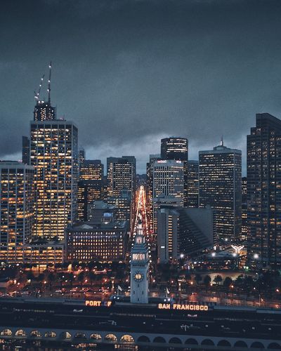 Illuminated buildings against cloudy sky at dusk