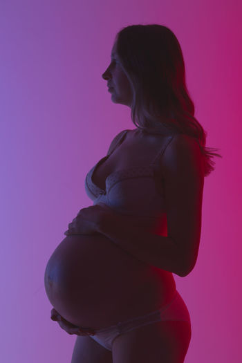 Side view of woman standing against pink background