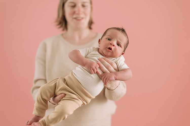 Photo of a newborn baby held in hands by mom over pink background