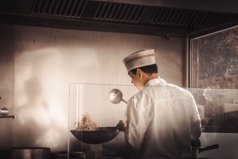Rear view of chef preparing food in commercial kitchen
