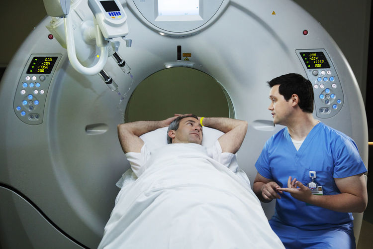 Patient lying on cat scan machine and talking to radiologist in hospital