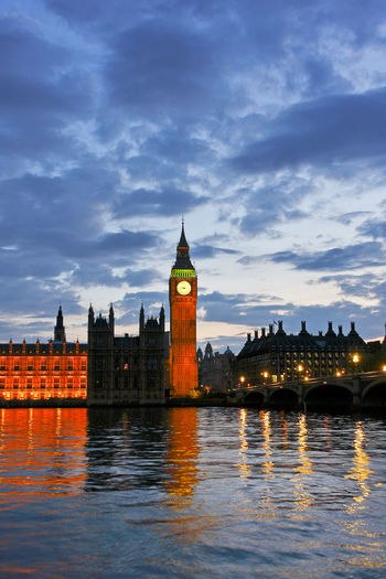 Illuminated  westminster buildings in london at waterfront against cloudy sky