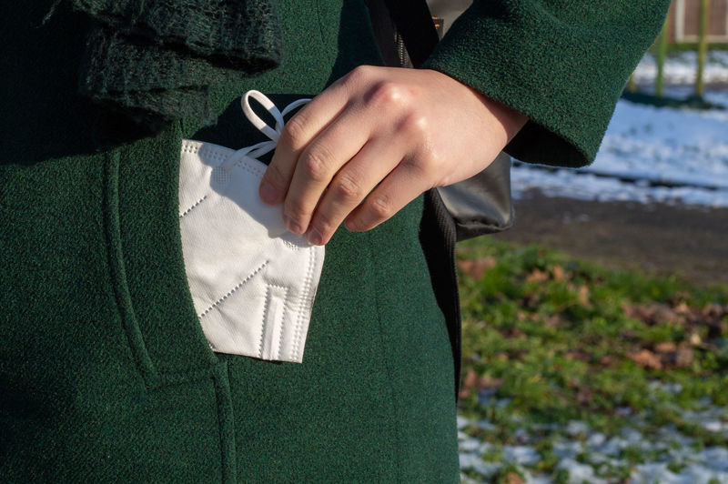 Midsection of woman holding mask from pocket standing outdoors