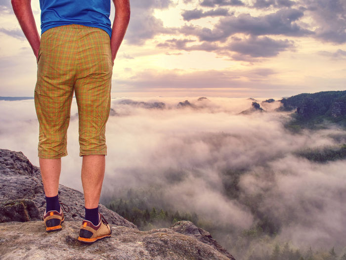 Sports casual man wearing outoor clothes and boots on rocky peak in sunny fall day. hands in pockets