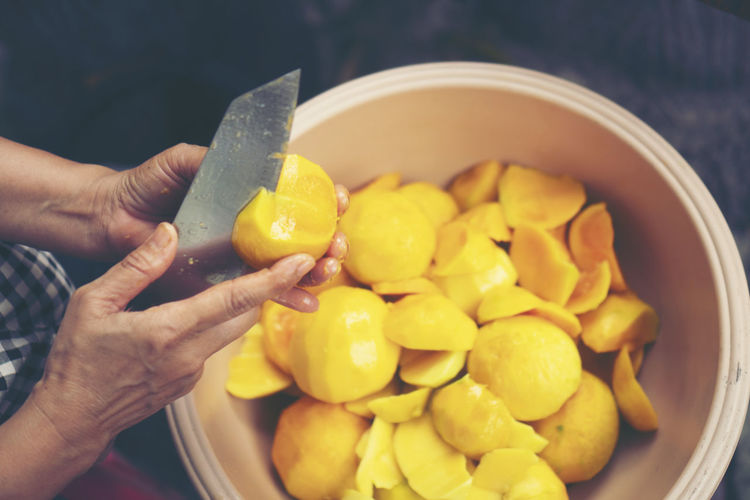 Cropped hands of person cutting mango fruit in container
