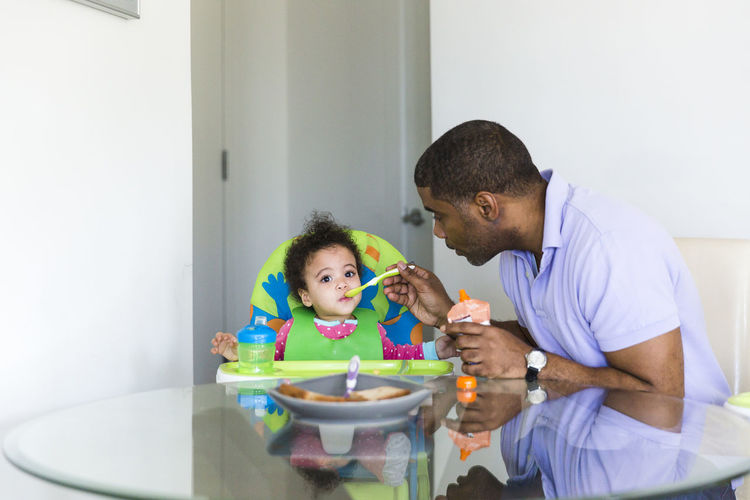Father feeding daughter while sitting at table