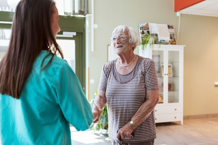 Smiling elderly woman shaking hands with nurse at nursing home