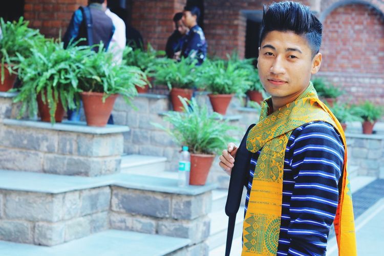 Portrait of young man standing against potted plants