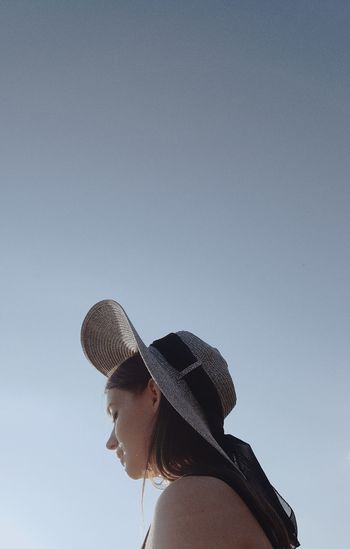 Low angle view of woman wearing hat sitting against sky