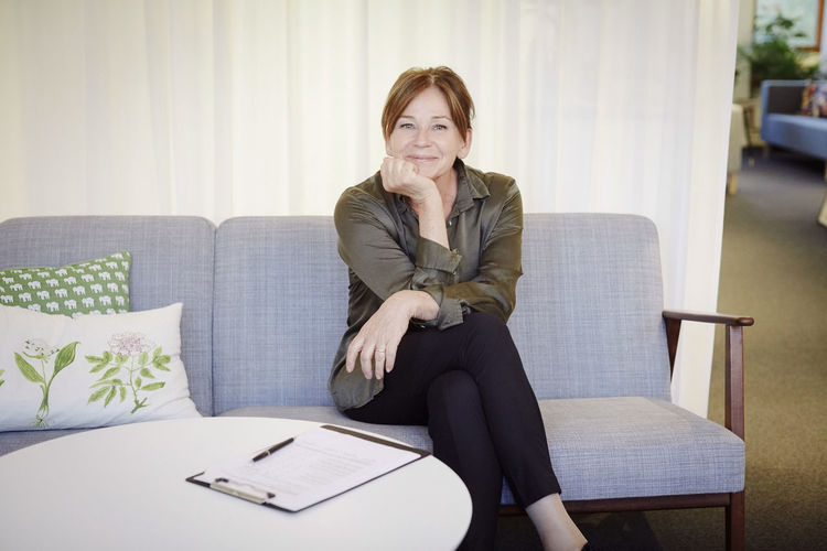 Portrait of confident smiling female psychologist sitting on sofa at workshop