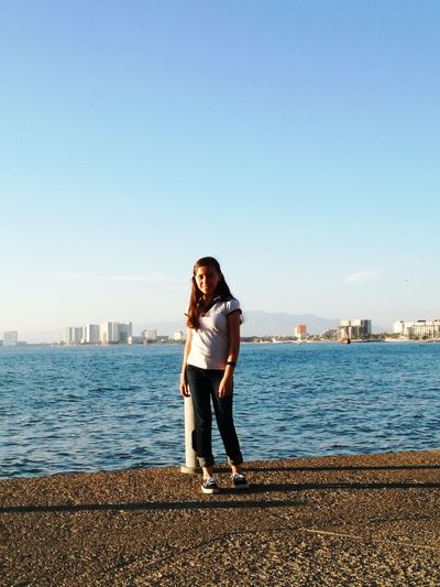 Portrait of teenage girl standing at promenade against blue sky