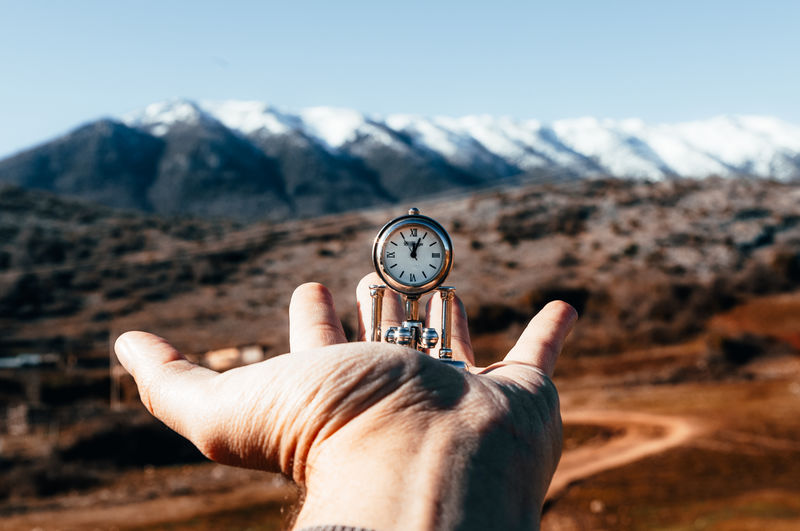 Midsection of person holding clock against mountain range