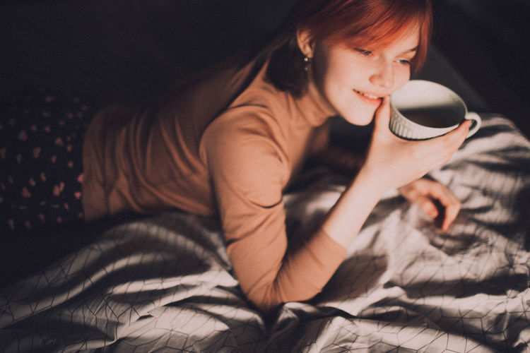 High angle view of girl holding coffee while lying on bed