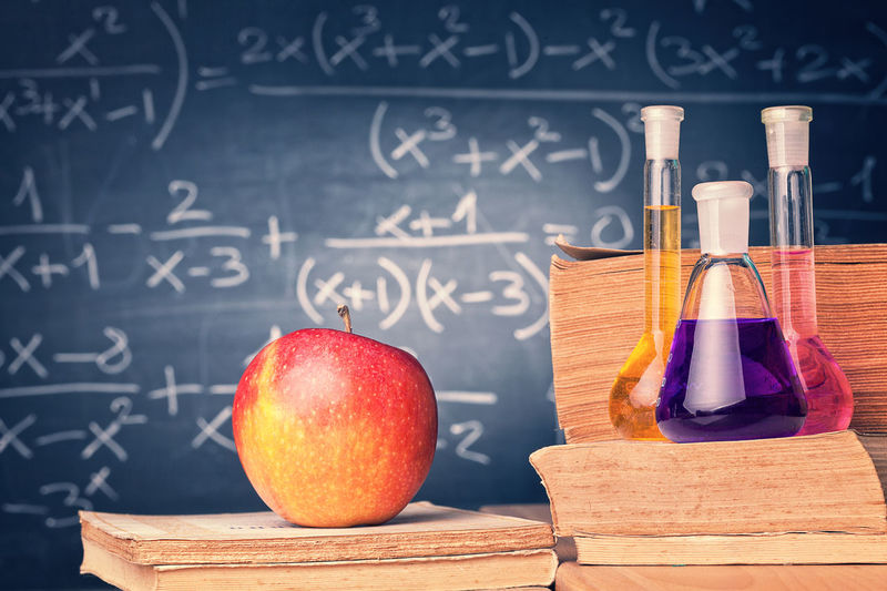 Close-up of apple with liquid in flasks on books against blackboard