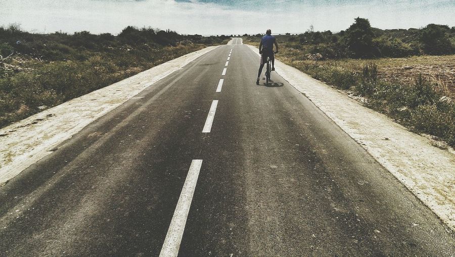 Rear view of man bicycling on country road