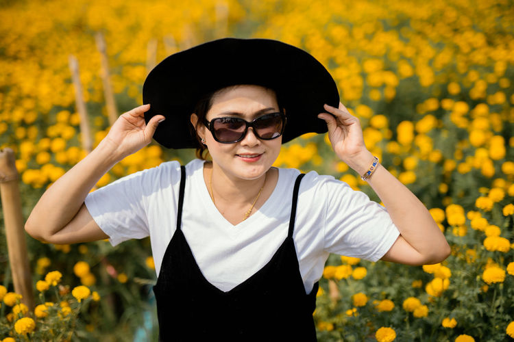 Smiling woman wearing hat and sunglasses while standing amidst plants