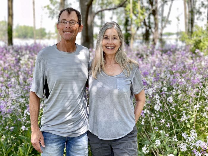 Portrait of a smiling woman with man outdoors against lilac spring flowers and river. 