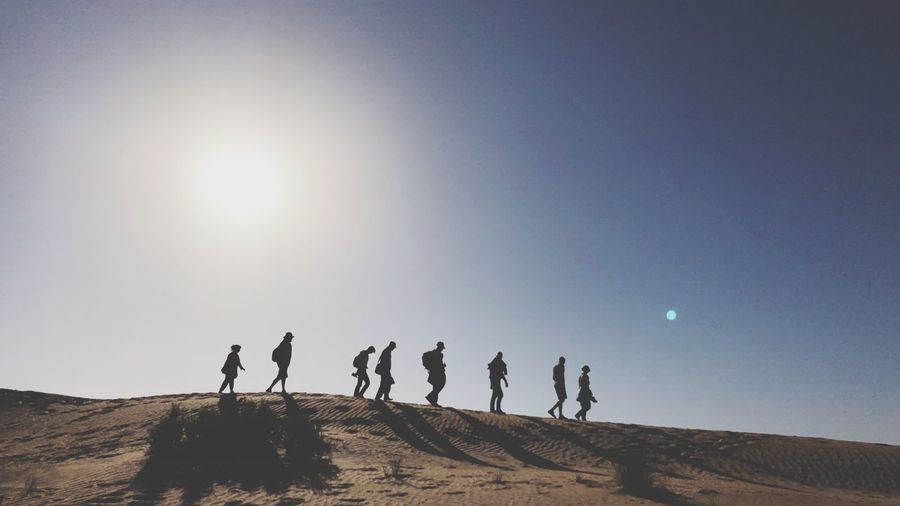 Silhouette people walking at desert against clear sky