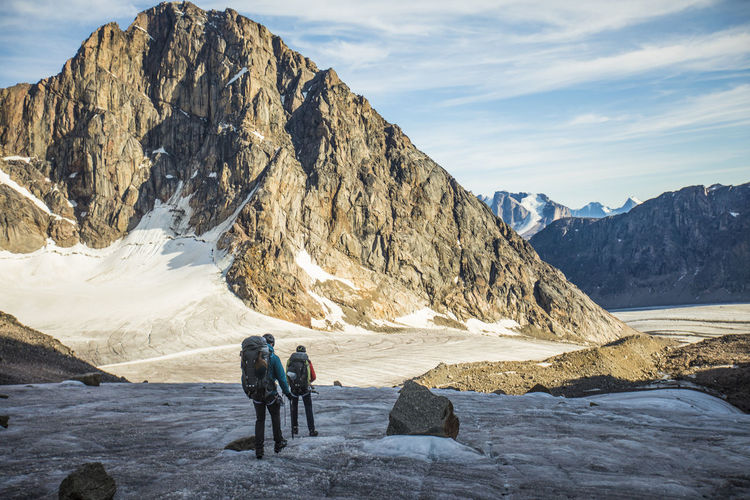 Two backpackers cross a glacier below mountain range.