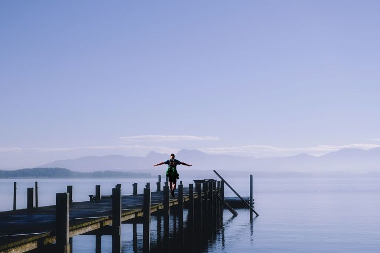 Rear view of woman standing on pier over sea against sky
