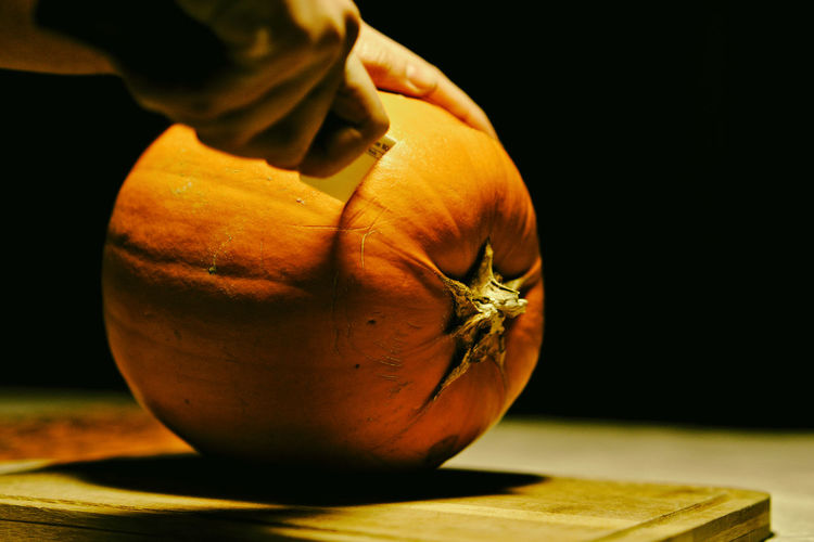 Cropped hand of person cutting pumpkin during halloween