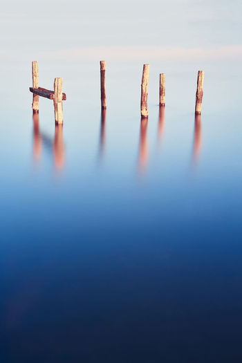 Wooden posts in water against sky