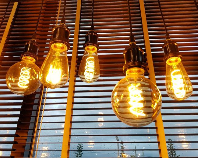 Low angle view of illuminated light bulbs hanging by window