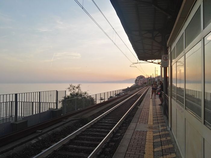Railroad station platform against sky during sunset