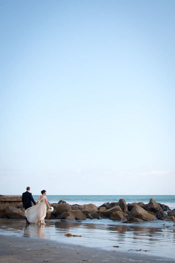 Full length of newly wed couple standing on shore at beach against sky