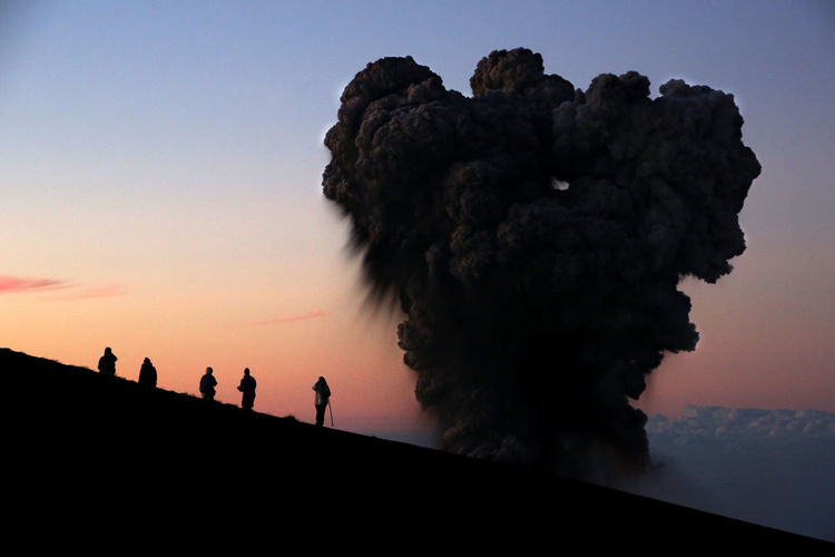 Low angle view of silhouette people and smoke against clear sky during sunset