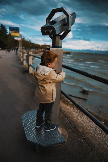 Full length of boy standing by coin-operated binoculars looking at sea