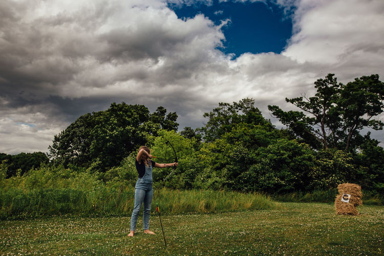 Woman standing by tree on field against sky
