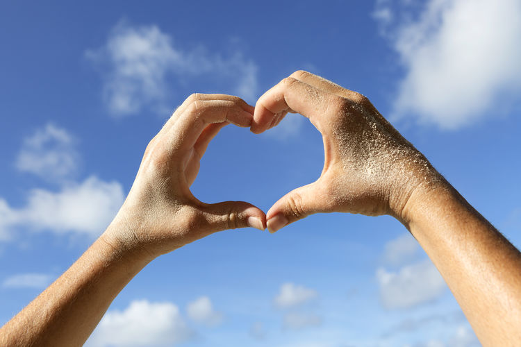 Close-up of woman hand holding heart shape on beach against sky