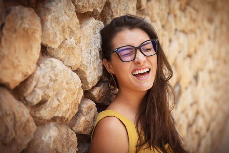 Portrait of young woman wearing sunglasses while sitting on rock
