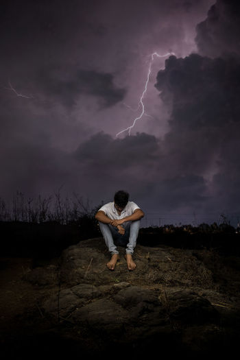 Man sitting on rock against sky at night