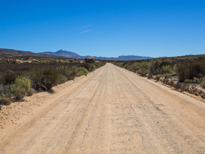 Empty dirt road amidst landscape against clear blue sky, cederberg national park, south africa