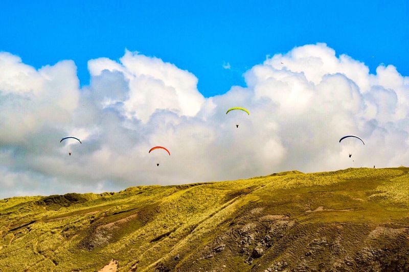 Scenic view of cliffs against sky with paragliders 