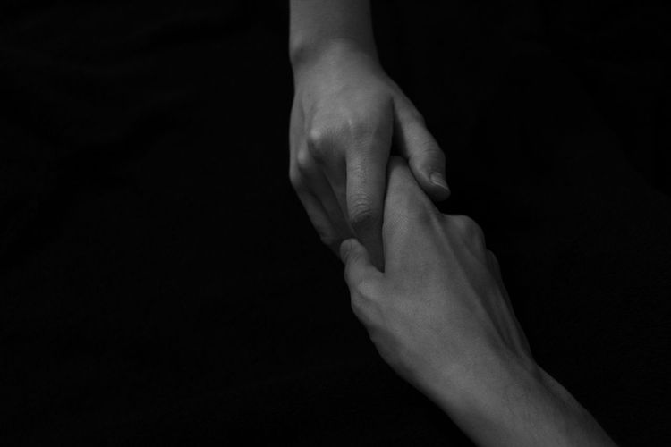 Cropped image of people holding hands against black background