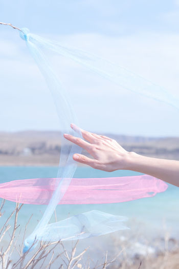 Cropped hand of woman with arms raised at beach against sky