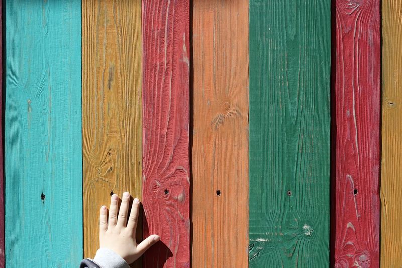 Cropped hand of child touching colorful painted wooden wall