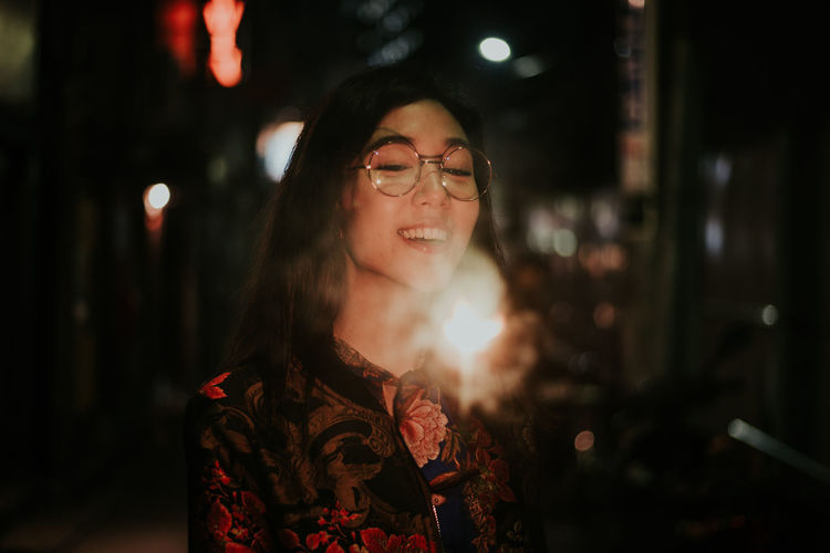 Smiling young woman holding sparkler at night