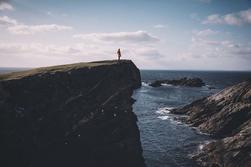 Woman standing on rocky shore against the sky