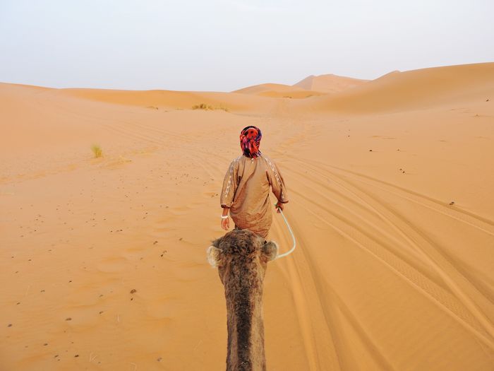 Man standing on sand dune in desert against sky